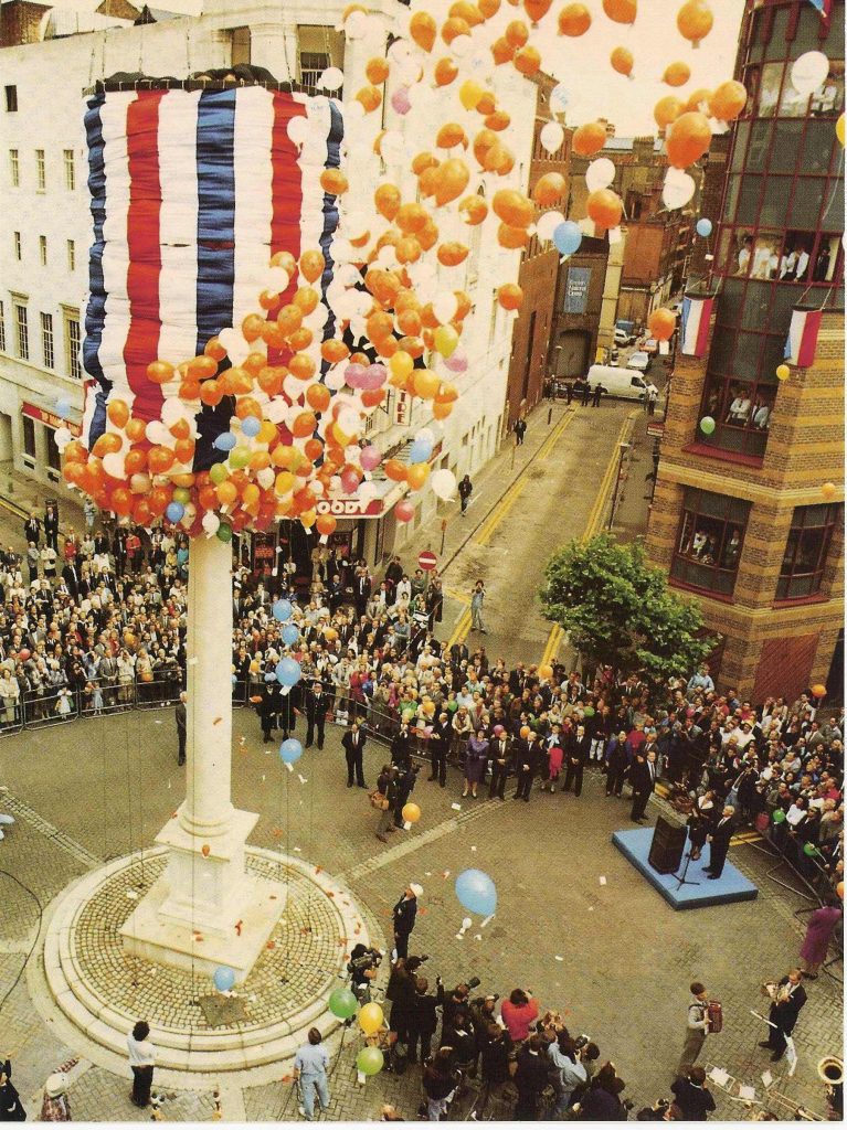 Photograph of the unveiling of the reconstructed Sundial Pillar by Queen Beatrix of the Netherlands in 1989. A shroud in the Dutch national colours is being lifted, releasing balloons.